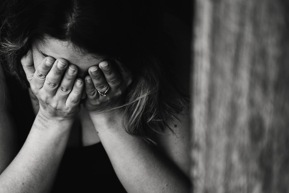 A person covering their face with both hands, expressing distress or sadness, in black and white.