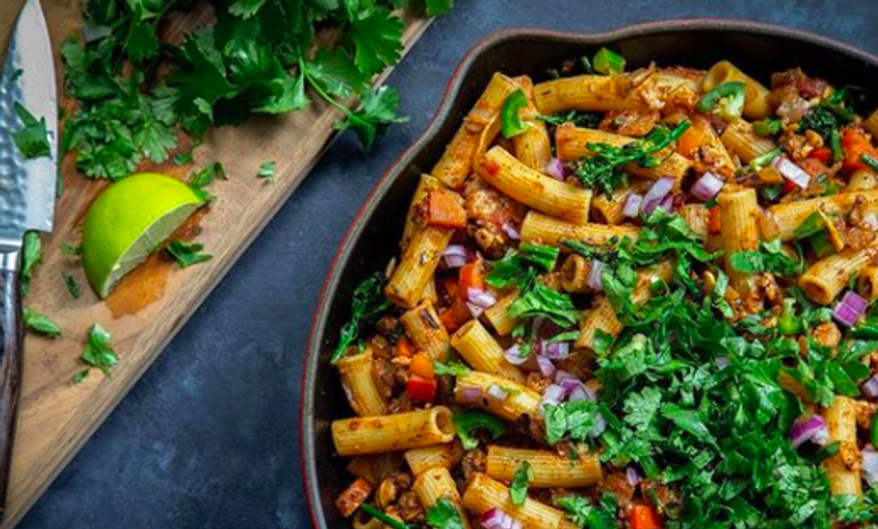 cutting board with cliantro, lime, and knife on it next to skillet of pasta with cilantro and onions on it