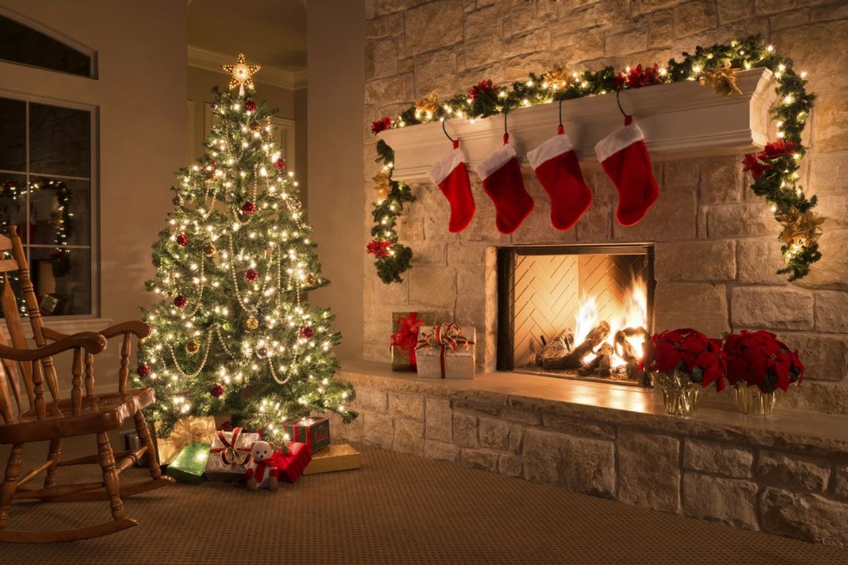 Cozy room with decorated Christmas tree, lit fireplace, stockings, and presents.